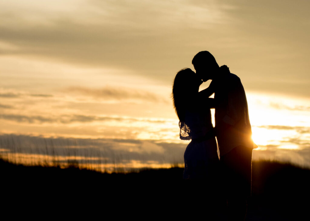 Silhouette of couple kissing in front of beach sunset.