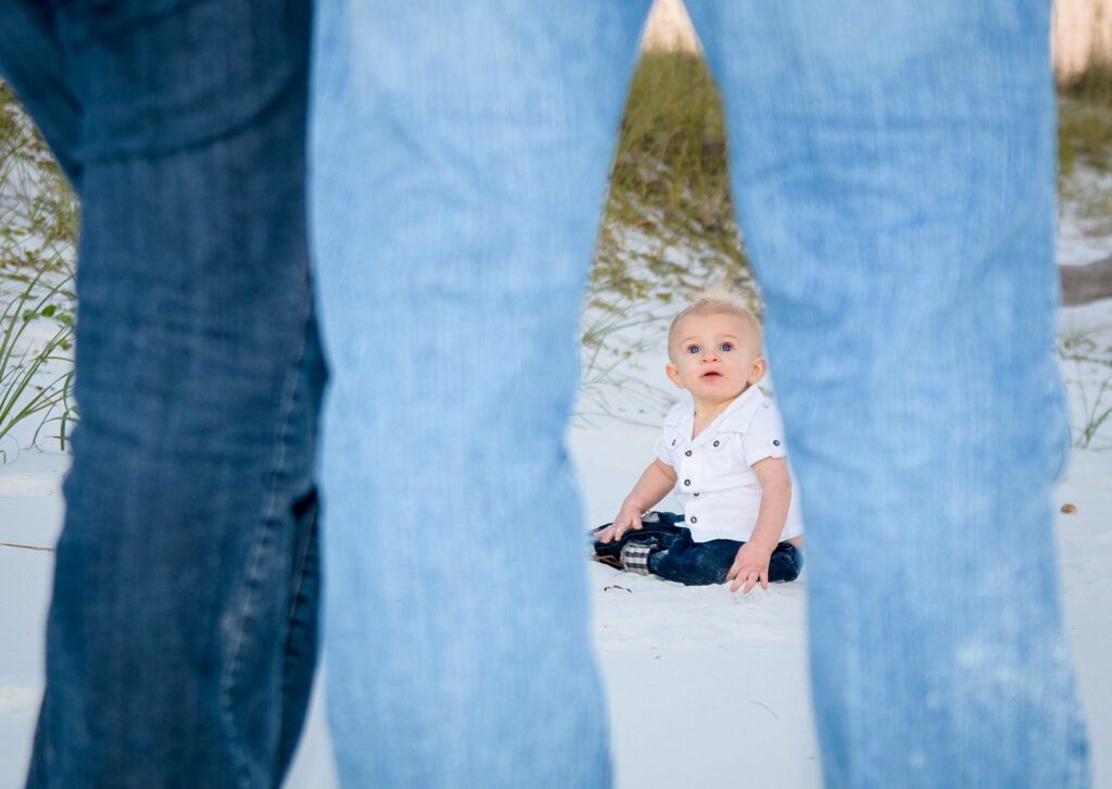 Baby sitting on beach looking at parents