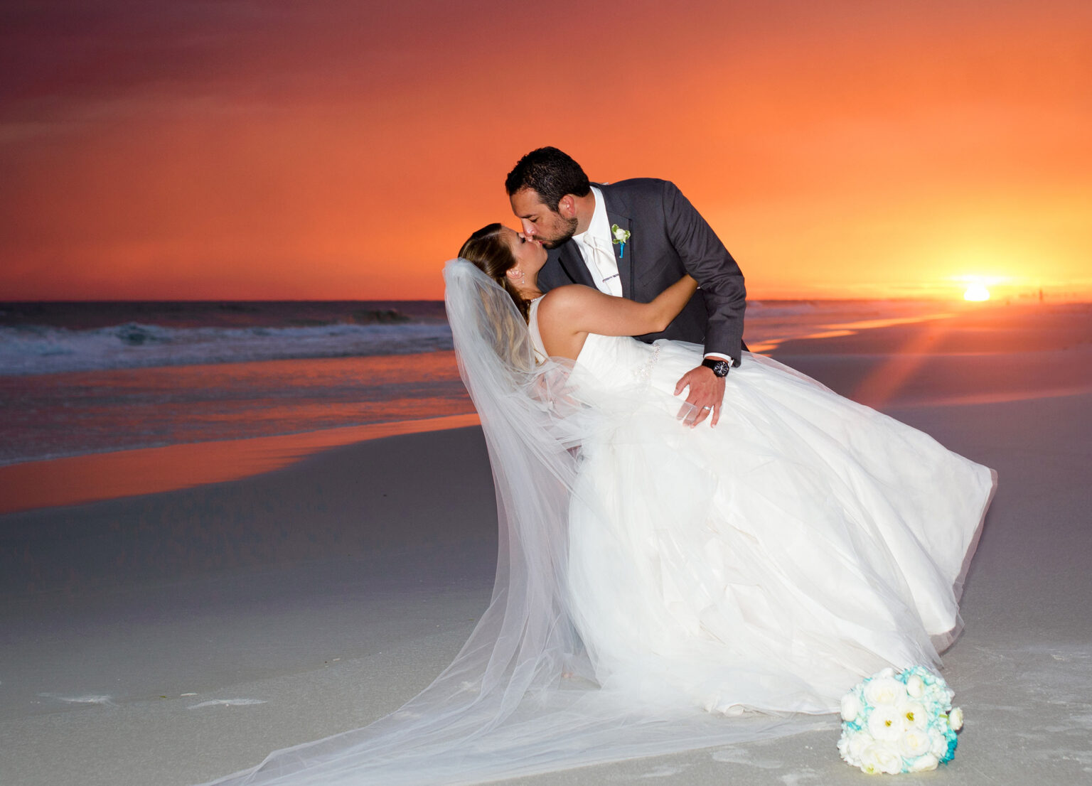 Bride and groom kissing in front of stunning beach sunset