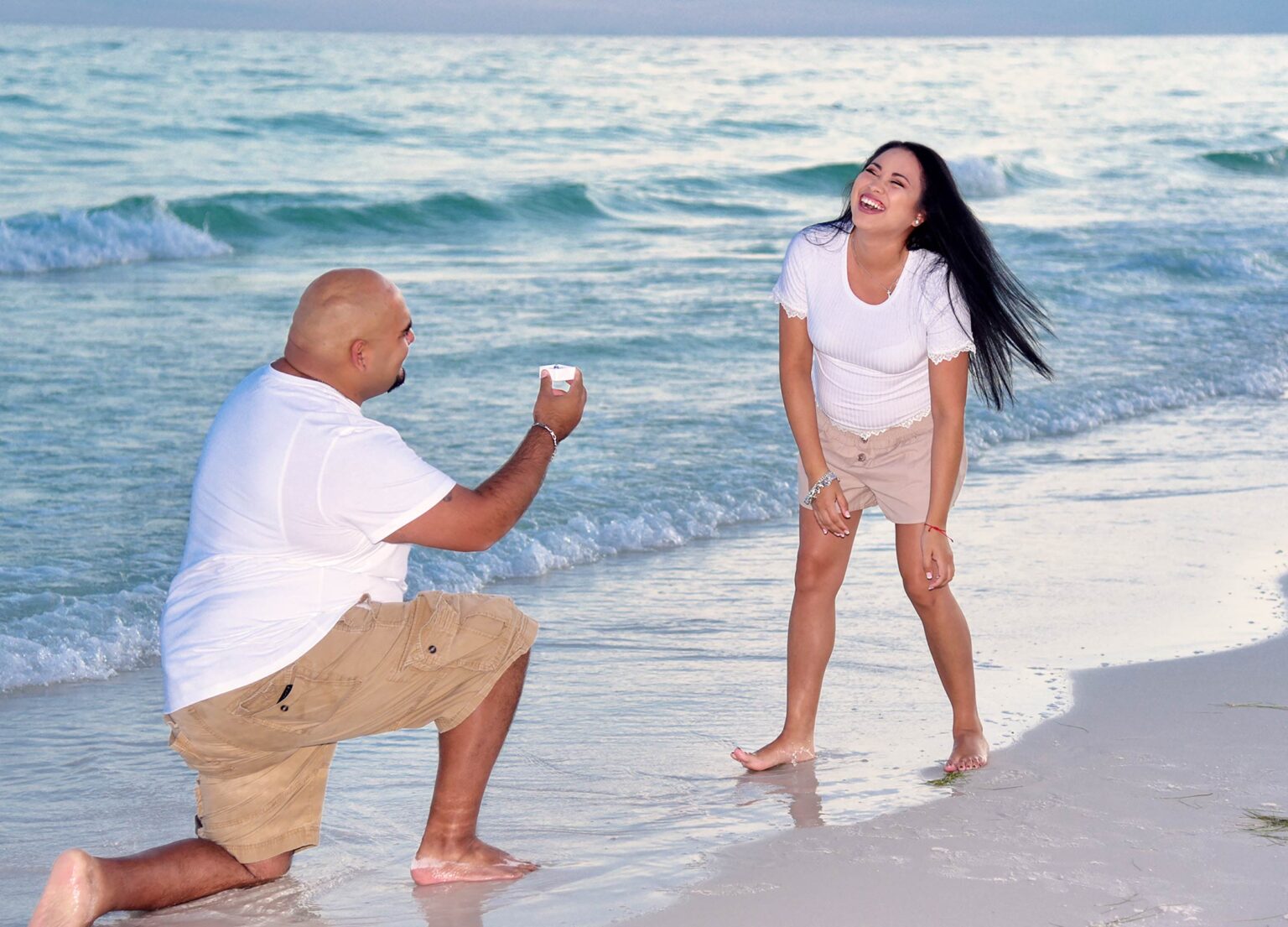 Man proposing to smiling girl on the beach at sunset