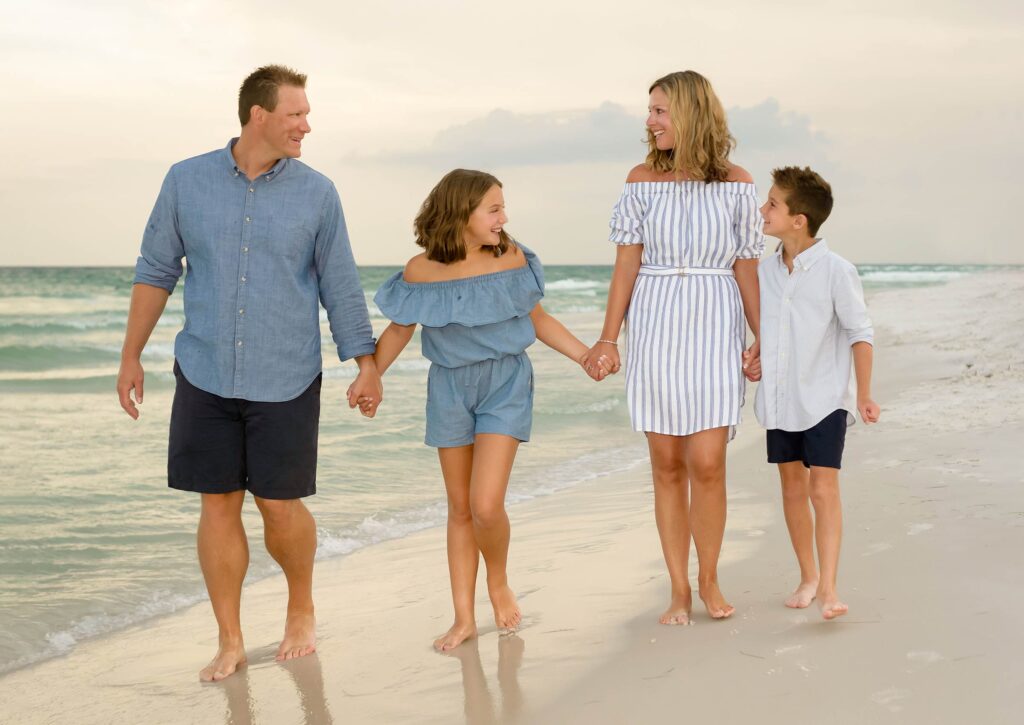 Family in coordinating outfits walking on Destin beach at sunset.