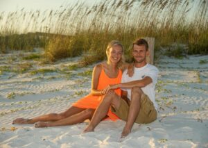 Newly engaged man and woman sitting by dunes and sea oats