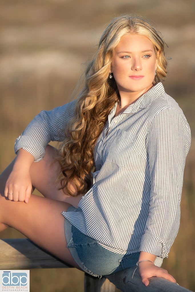 Girl sitting in front of dunes for Senior Photos at the beach